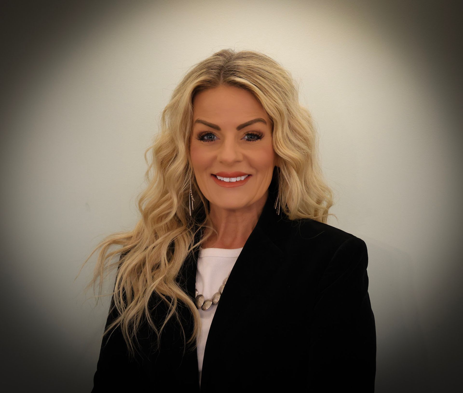 Portrait of a smiling woman with long blonde hair in a black blazer against a gray background