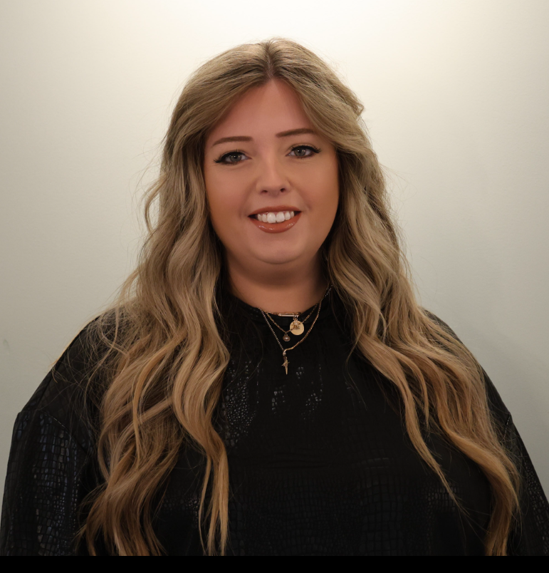 Woman with long wavy blonde hair wearing a black top, smiling against a plain light background