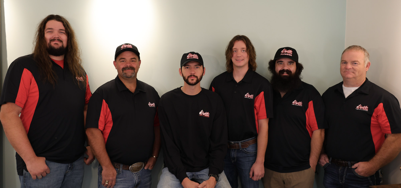Six people in black and red branded shirts standing indoors against a plain wall