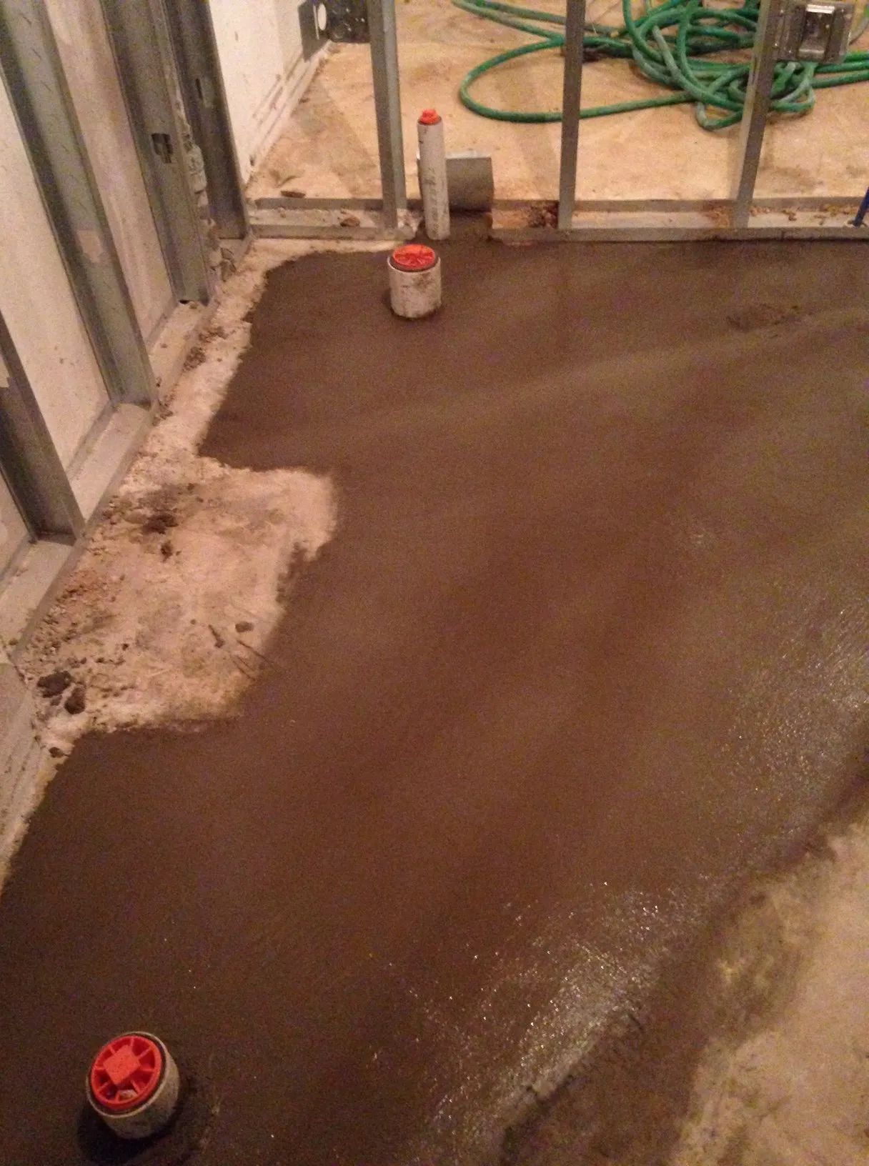 Freshly poured brown concrete floor in an unfinished room with tools and pipes nearby