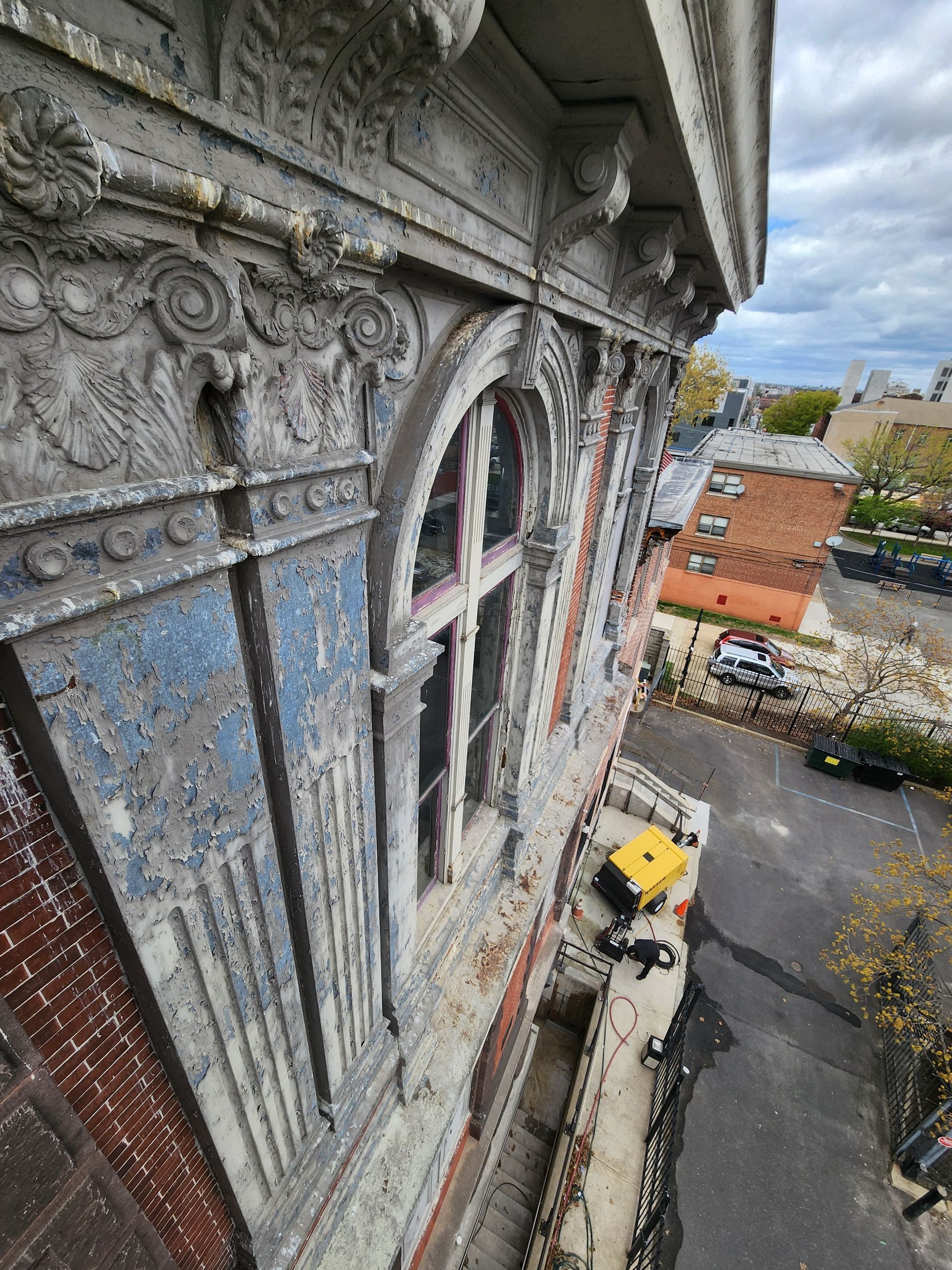 High-angle view from a stone building facade over a narrow street with parked cars and brick buildings below