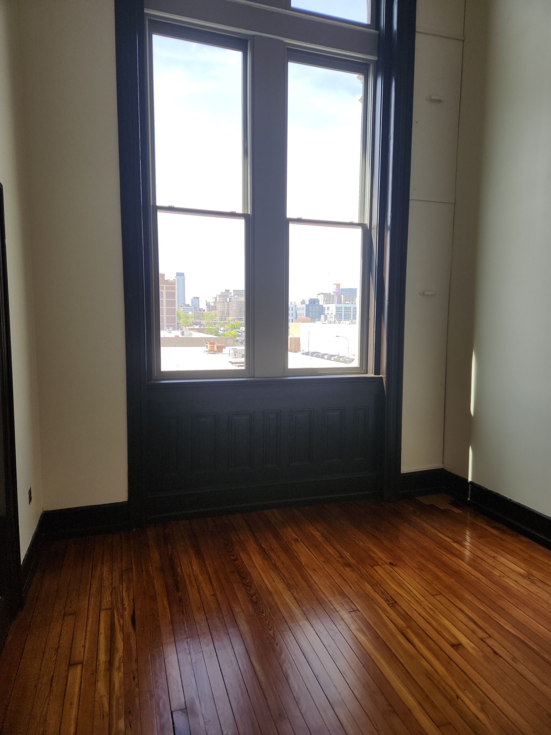 Empty room with dark wood floors and a large window overlooking a city street.