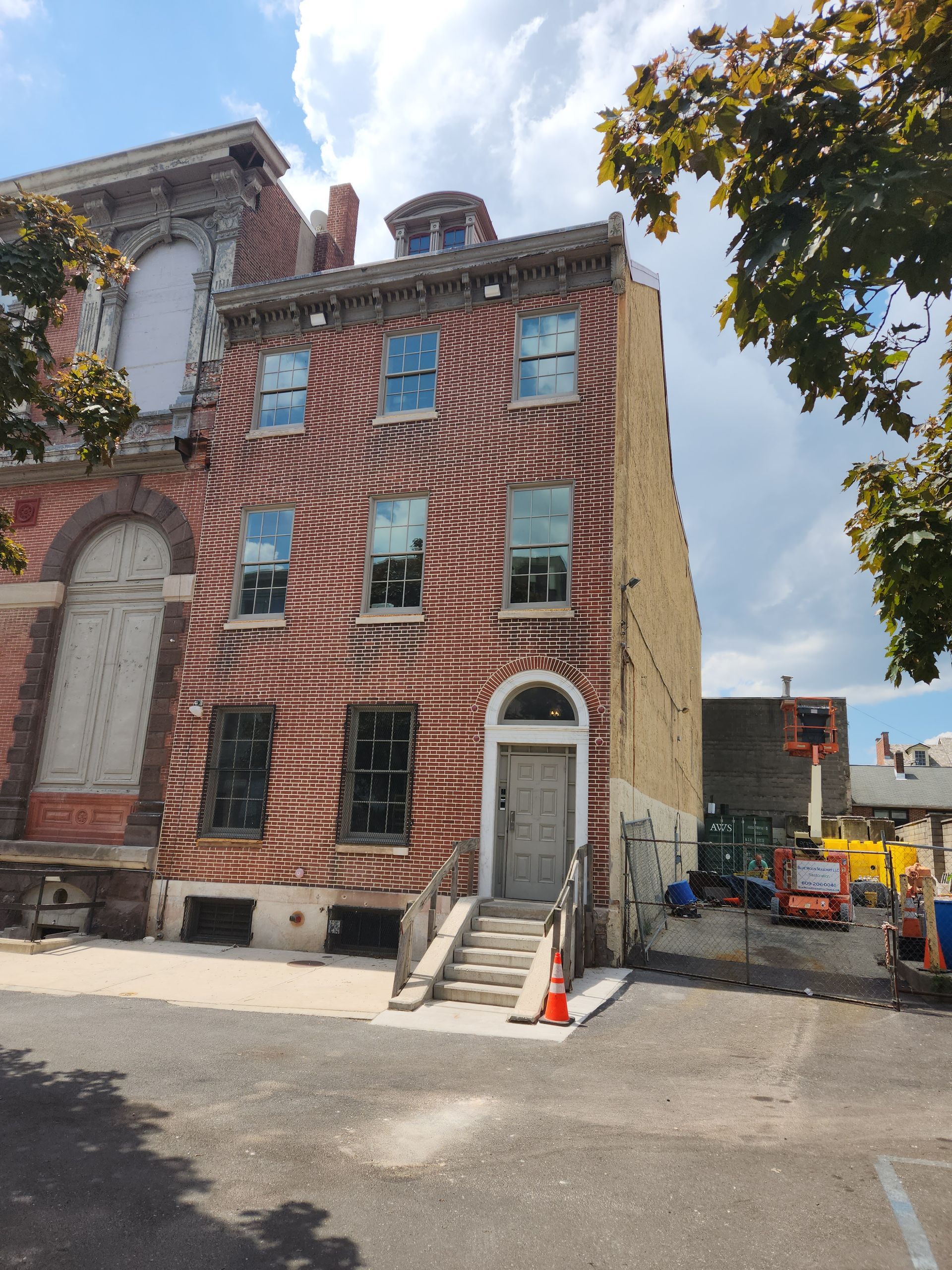 Brick townhouse corner building with white trim and front steps on a sunny street