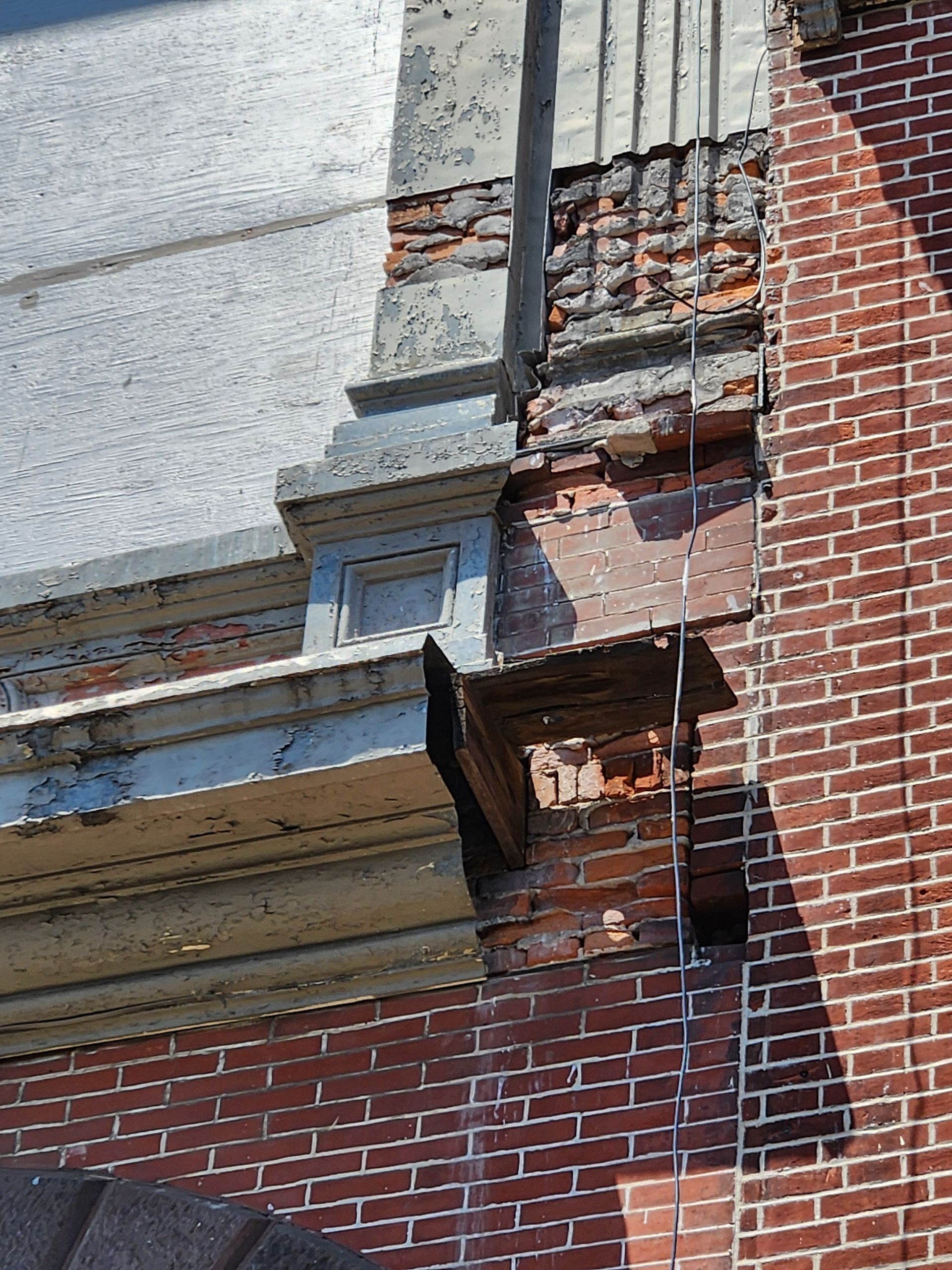 Close-up of a damaged brick and stucco building facade with exposed masonry and a broken decorative ledge