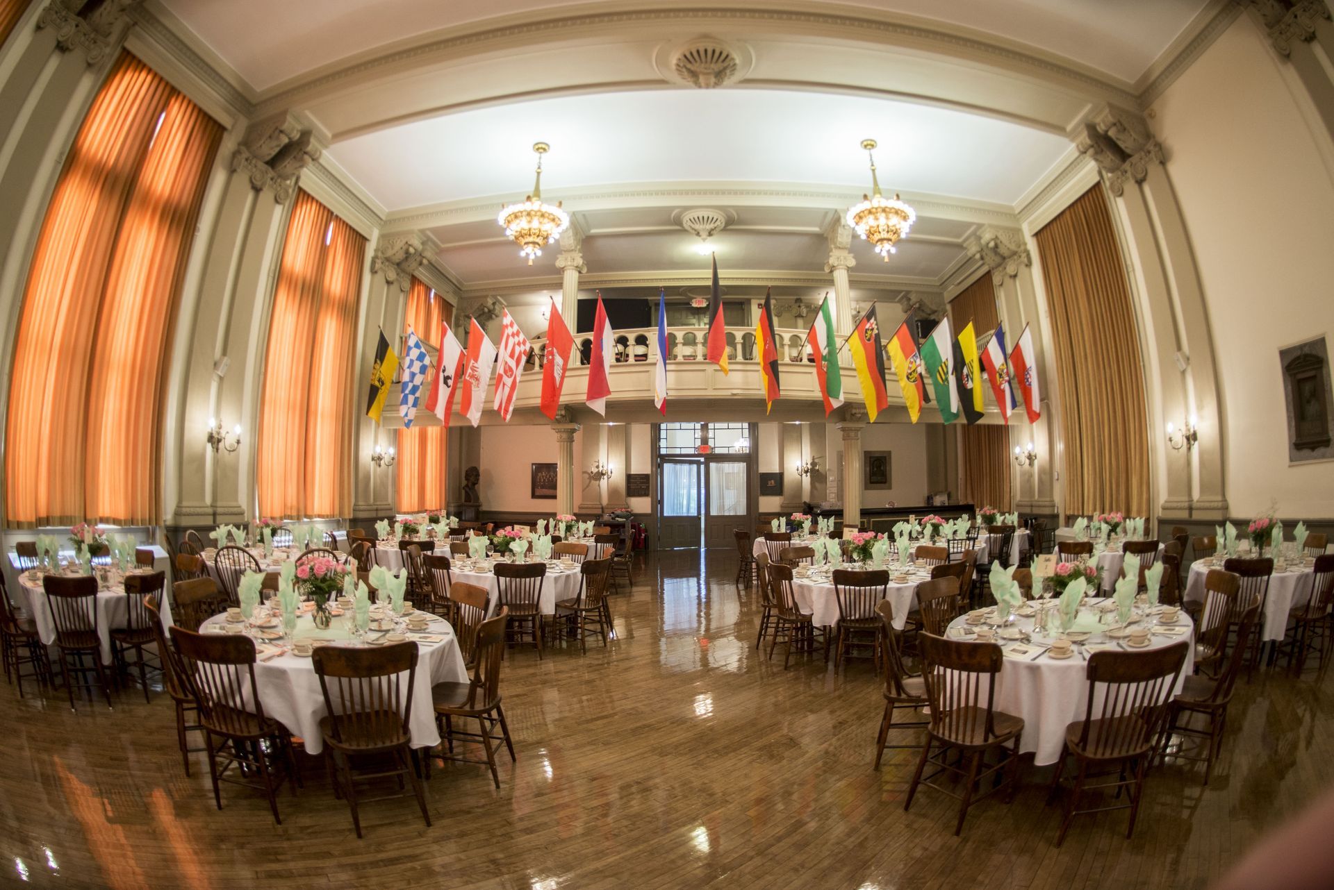 Elegant banquet hall with round tables, white chairs, chandeliers, and rows of colorful international flags