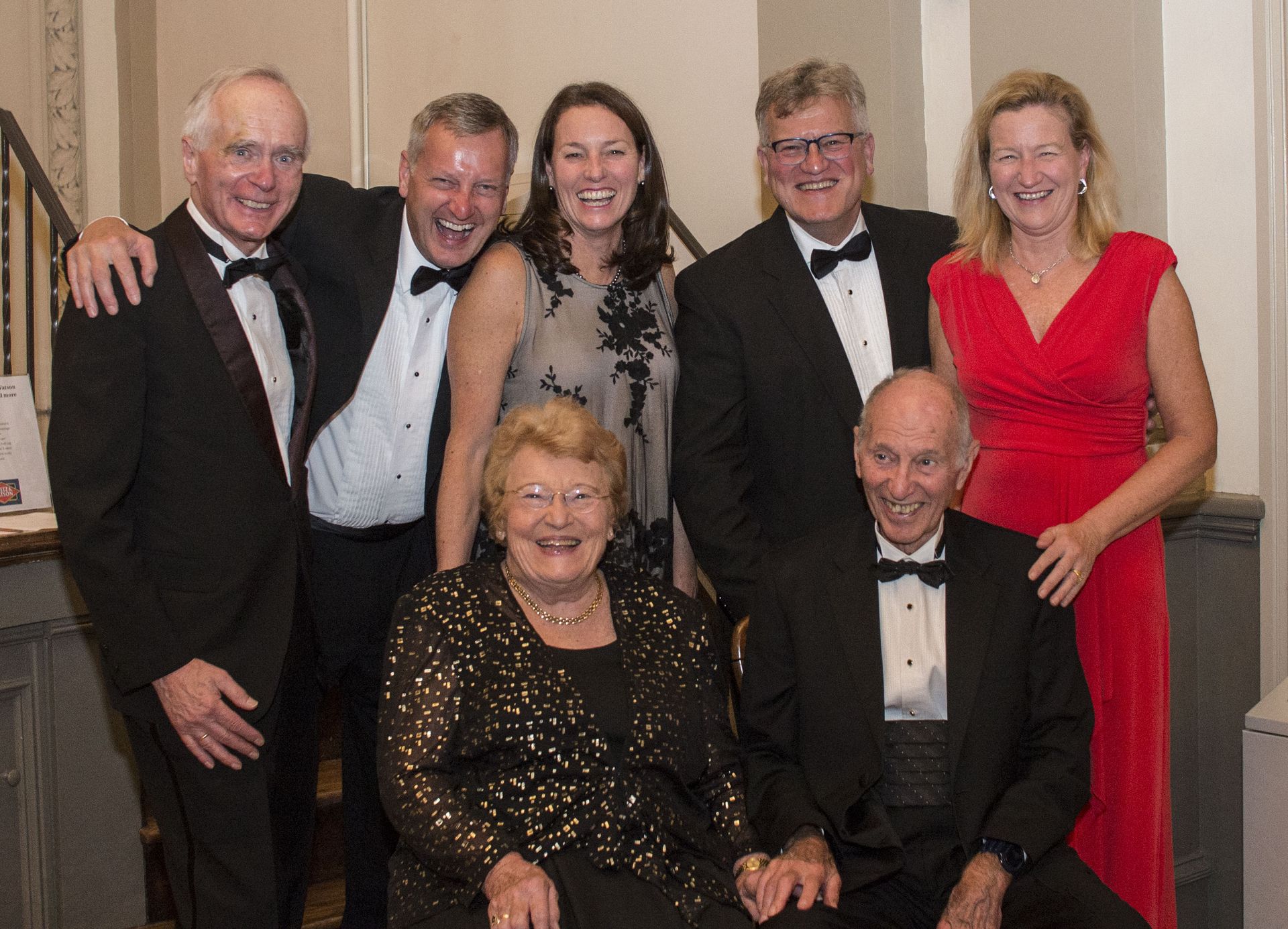 Six formally dressed people posing indoors, smiling at a celebration event.