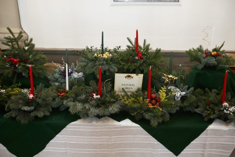 Holiday floral arrangement with red candles and greenery on a white-draped table
