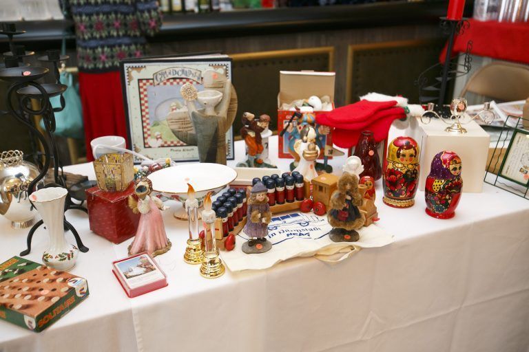 Table of assorted decorative dolls and collectibles at a market stall, with white tablecloth and colorful items.