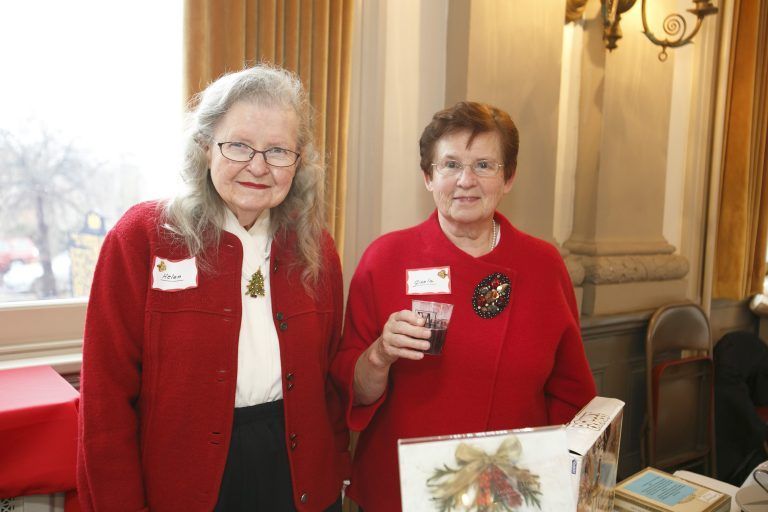 Two women in red jackets standing at a table with crafts in a warmly lit room