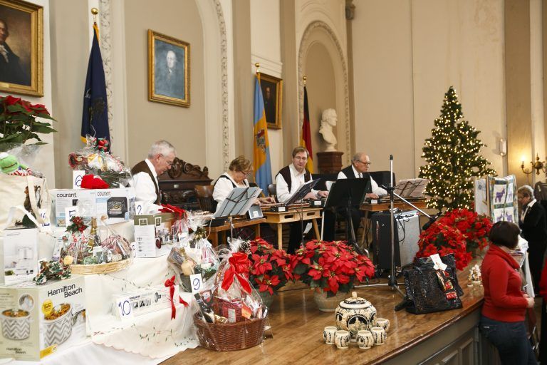 Musicians perform on a decorated church stage with Christmas trees and poinsettias during a holiday event