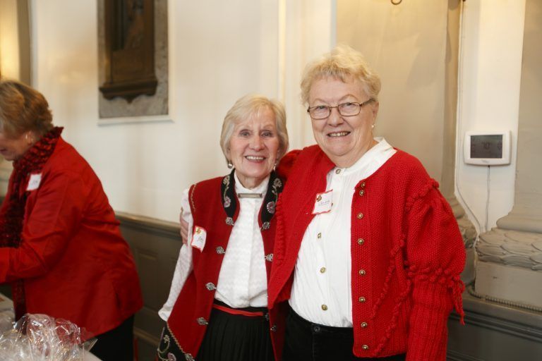 Two women in red sweaters smiling indoors at a formal event