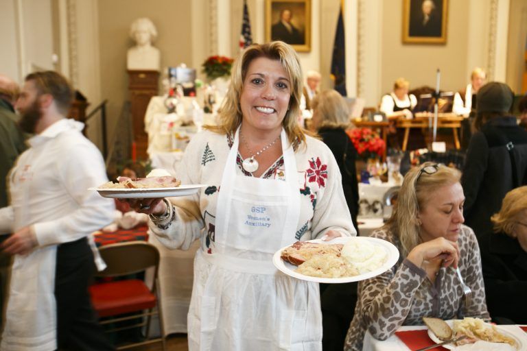 Woman in a white apron carrying plates of food in a busy restaurant room