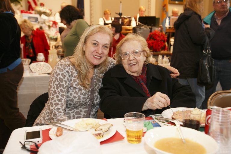 Two smiling people seated at a banquet table with food and drinks in a busy dining hall