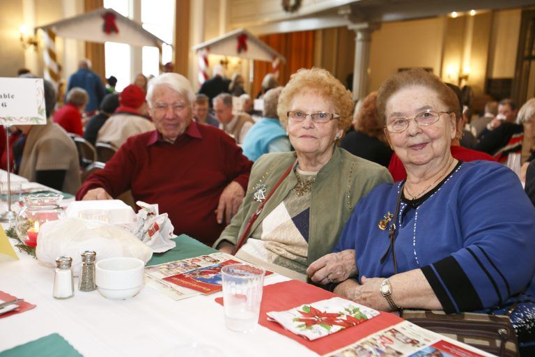 Three people seated at a decorated table in a bright indoor event hall, smiling toward the camera.
