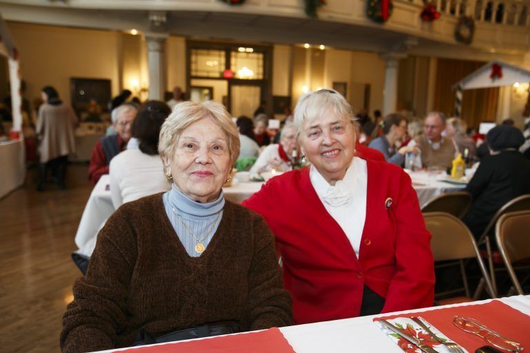 Two smiling seniors seated at a table in a decorated indoor gathering hall
