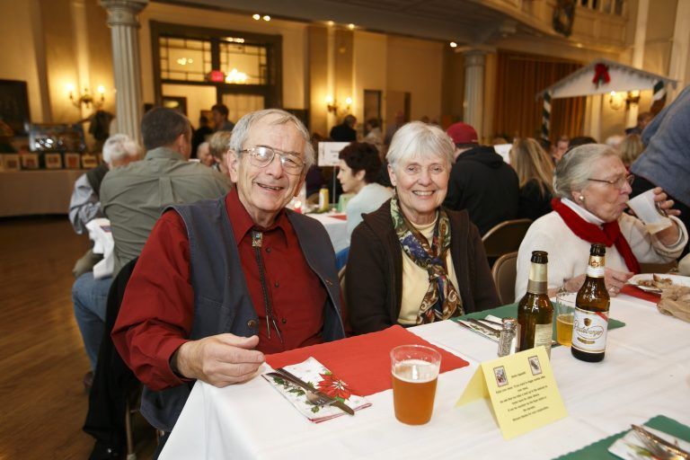 Two smiling diners at a table in a warmly lit banquet hall, with drinks and menus.