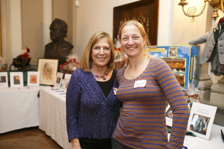 Two women smiling at an art exhibit with framed photos and a sculpture in the background
