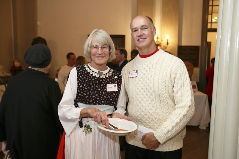 Two people posing indoors at a social event, holding plates and smiling.