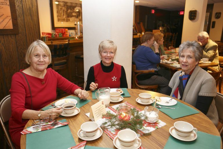 Three women seated at a café table with cups and desserts, chatting in a cozy restaurant