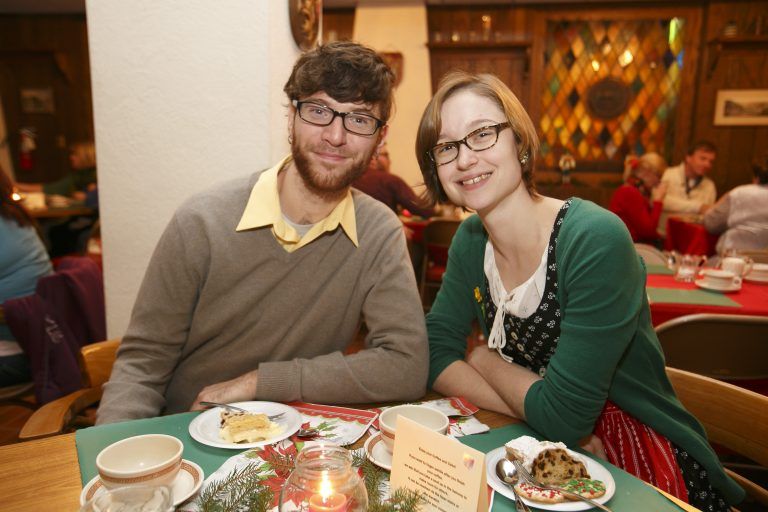 Two people seated at a restaurant table, smiling with plates and drinks in front of them.