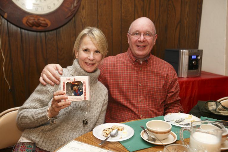 Two people smiling at a table, holding up a framed photo in a wood-paneled room.
