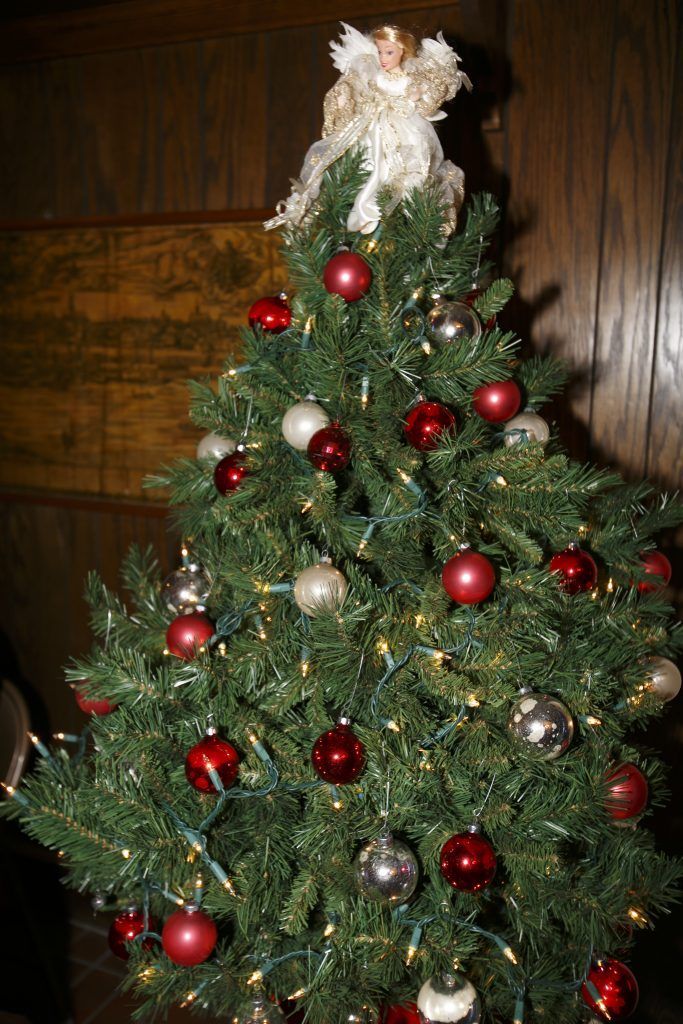 Small decorated Christmas tree with red and silver ornaments and a white topper, indoors.