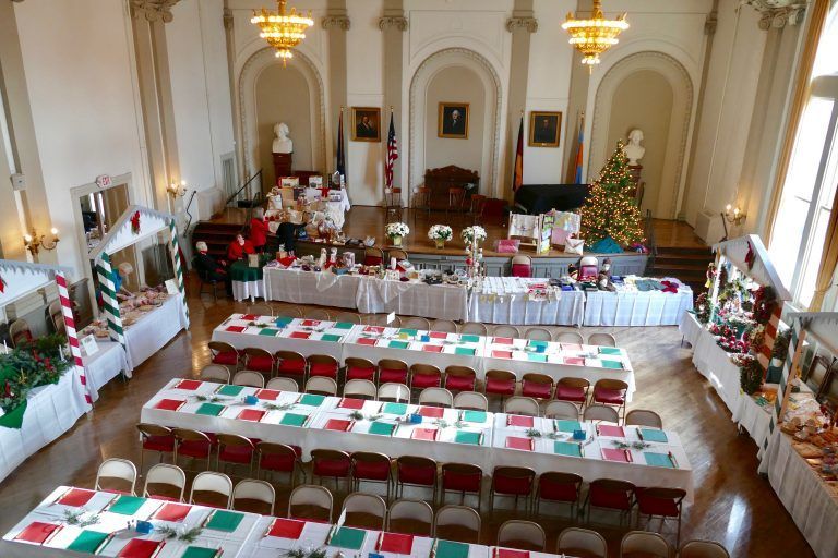 Banquet hall set for a formal event, with long tables, red chairs, and white tablecloths in a bright room