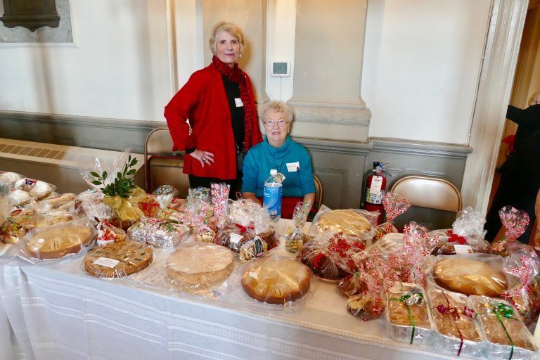 Two people behind a table of baked goods at a holiday-style bake sale