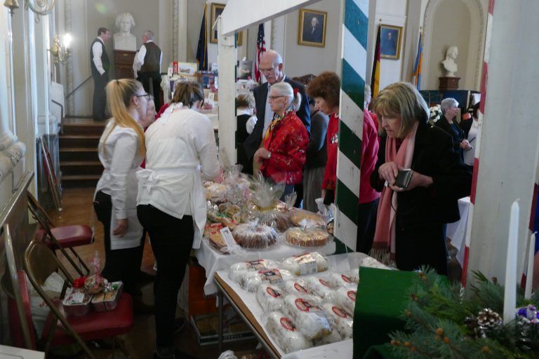 People browsing a display of baked goods and treats in a narrow indoor hallway.