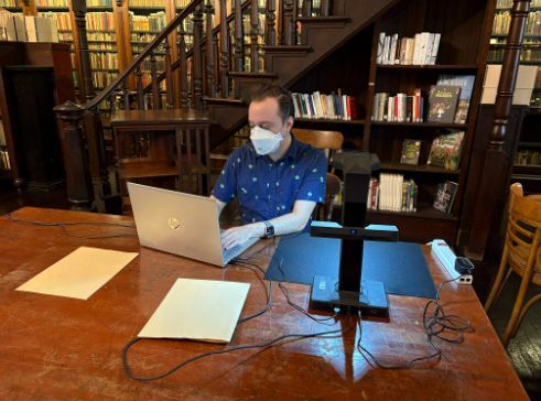 Masked person using a laptop at a wooden table in a library