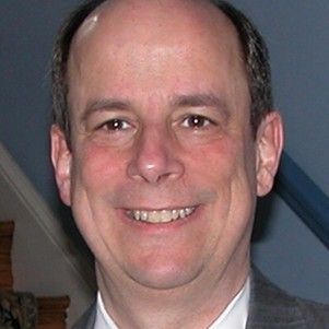 A woman wearing a gray jacket and a white shirt is smiling for the camera.