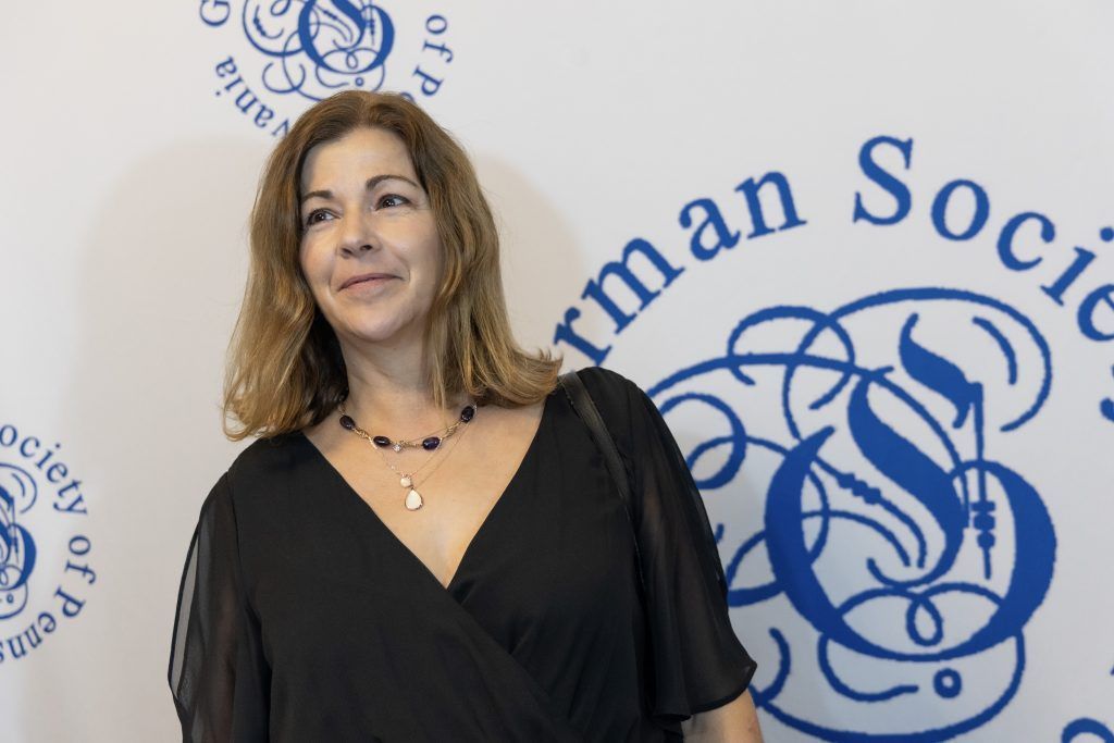 Woman in a black dress posing at a German Society event backdrop with blue logo text.
