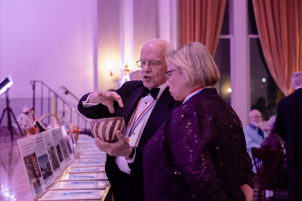 Two people conversing beside a display table at a purple-lit evening event