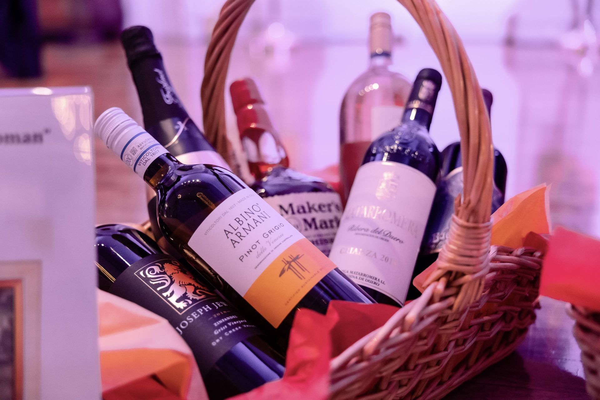 Basket of wine bottles with pink ribbons on display at an event table