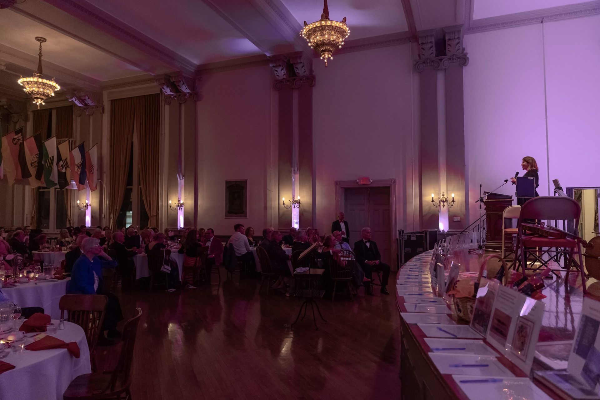 Elegant banquet hall with chandeliers, purple lighting, and seated guests at a formal event.
