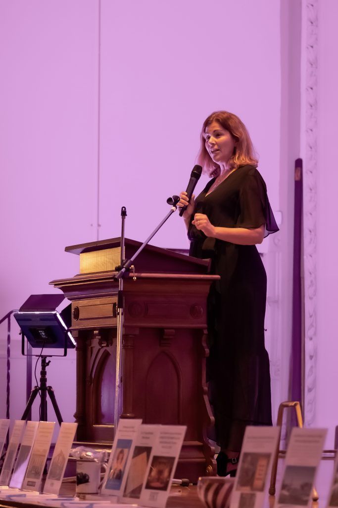Woman speaking at a podium in a purple-lit auditorium
