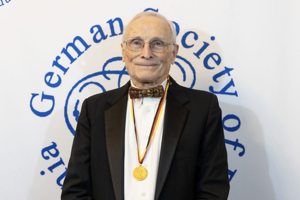 Man wearing a medal stands before a German Society backdrop