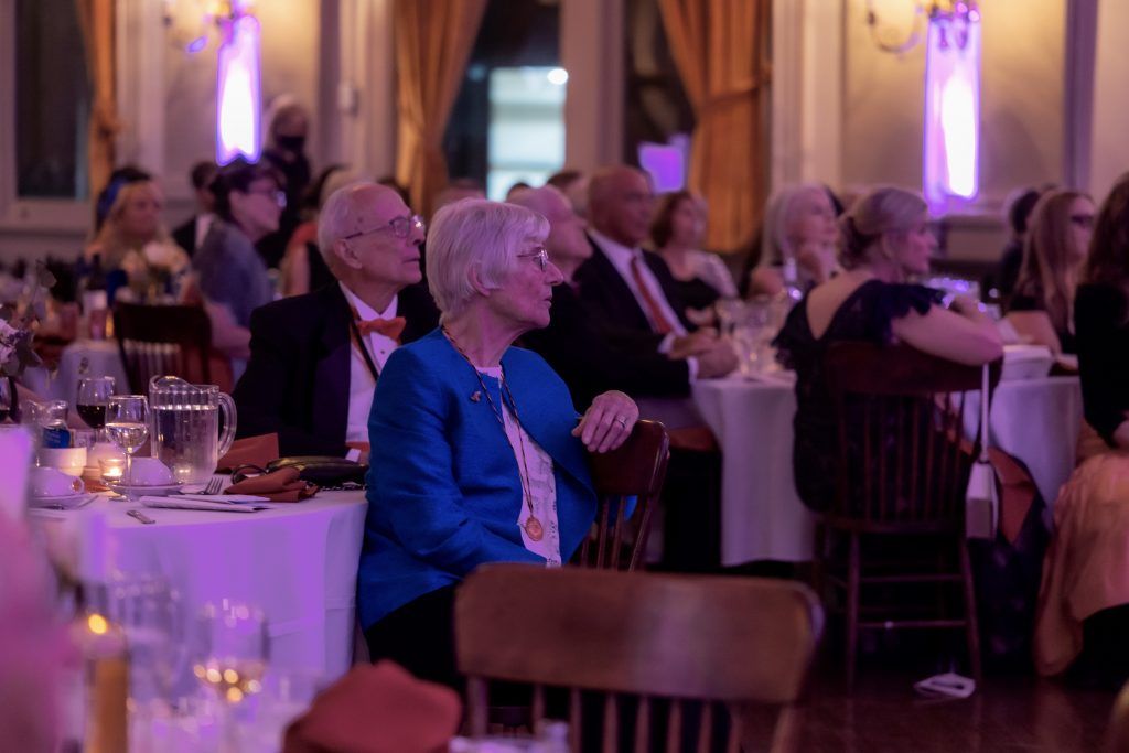 Guests seated at round tables in a softly lit banquet hall with purple lighting