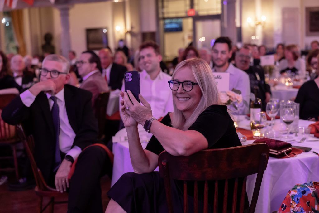 Audience applauding at a formal banquet, with a woman in glasses smiling in the foreground.