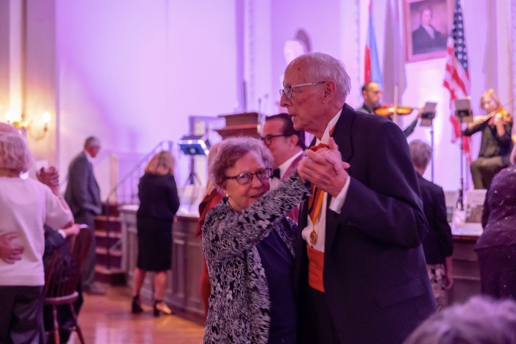 Couple dancing at a formal indoor event with purple lighting and flags in the background