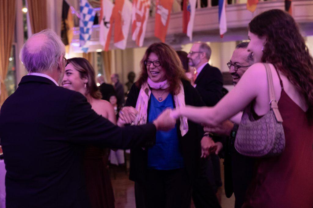 People dancing and mingling at a lively indoor party under pink-purple lighting