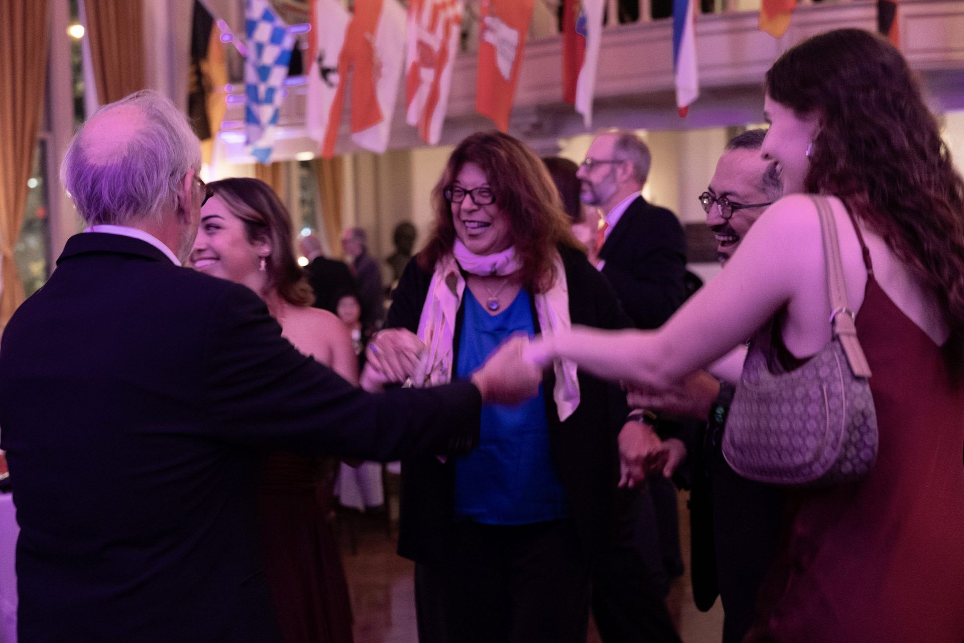 People mingling and greeting each other at an indoor party with flags and warm lighting.