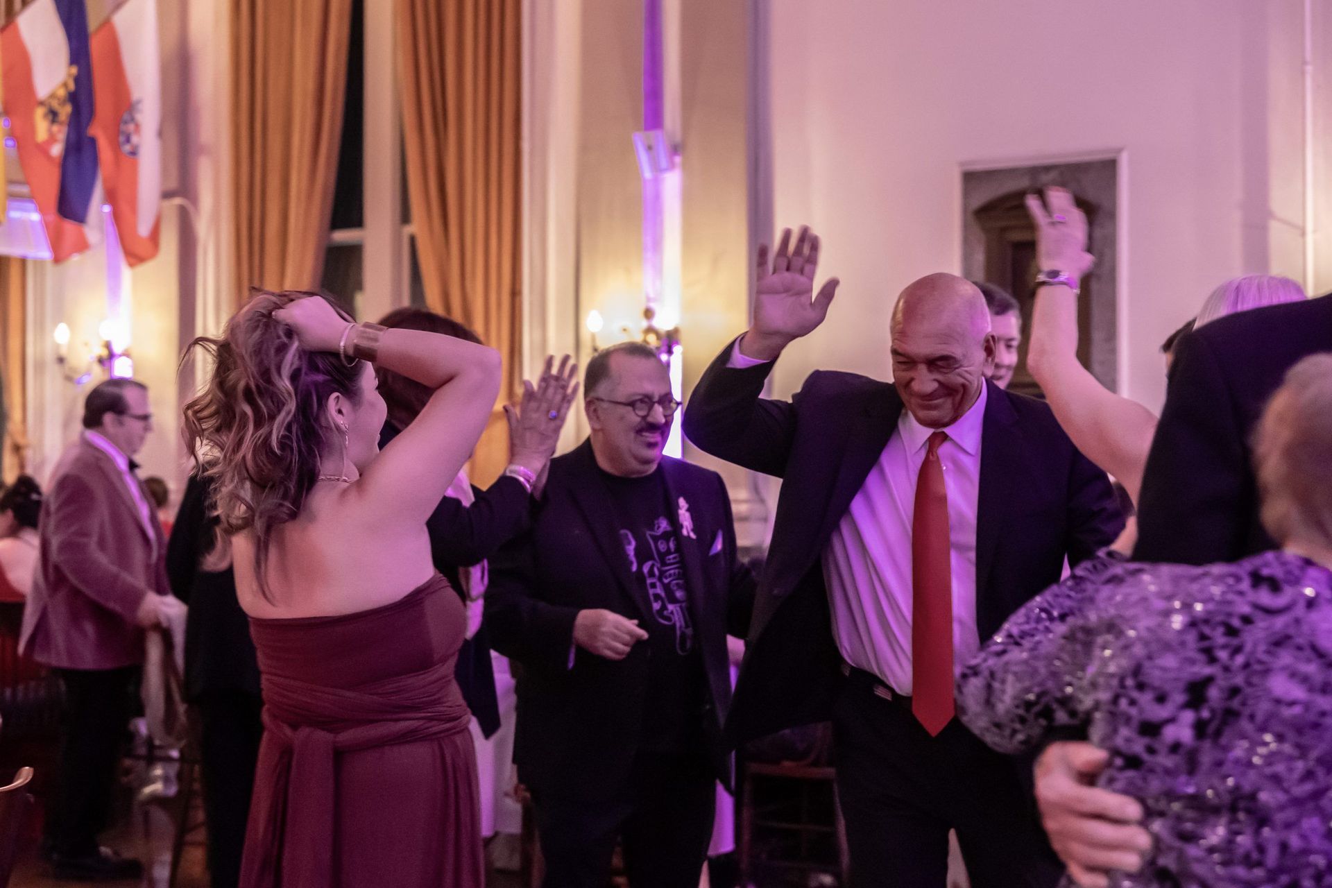 Guests dancing and raising their hands at a lively indoor event with purple lighting