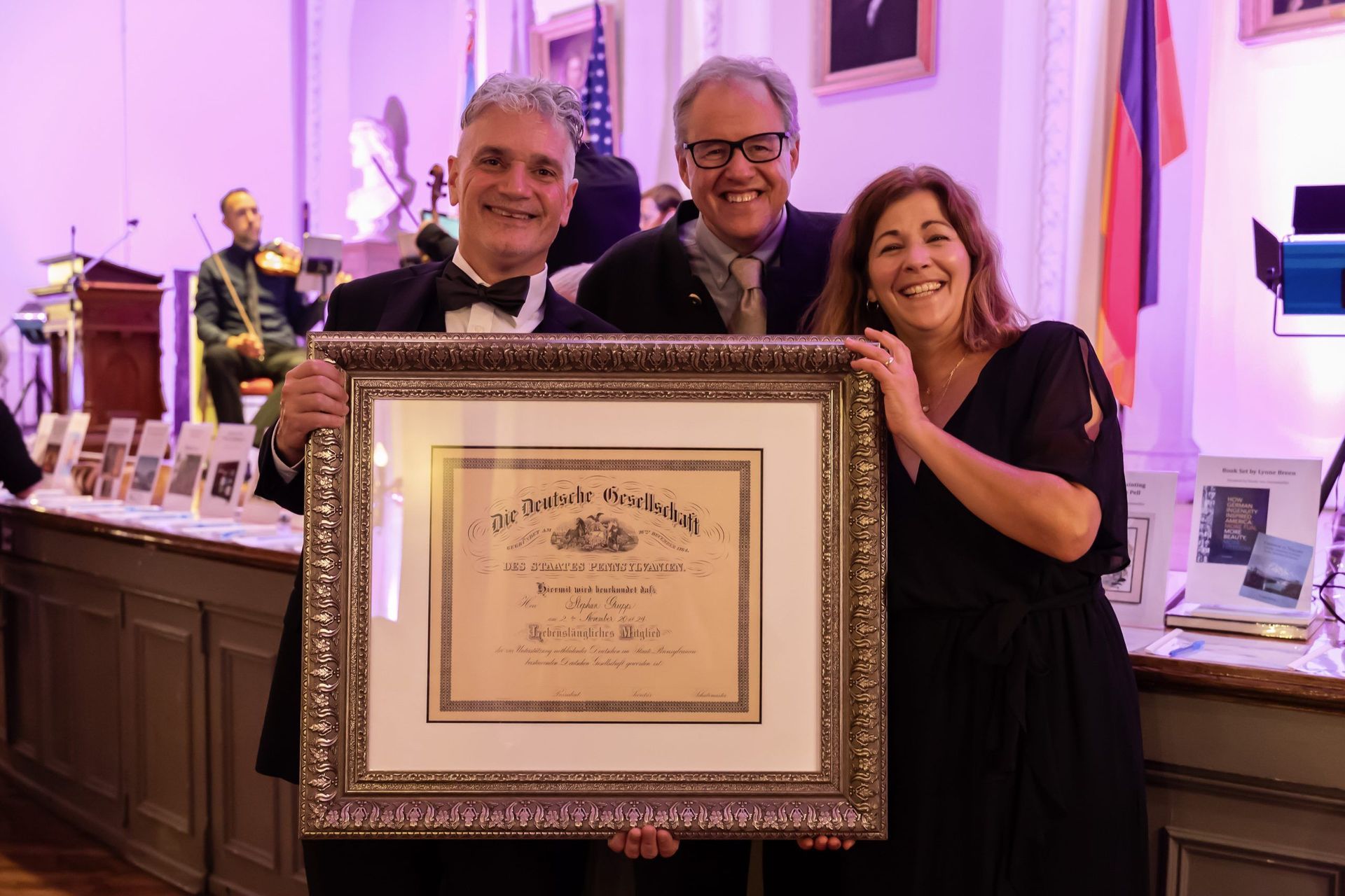 Three people holding a framed certificate at a formal indoor event