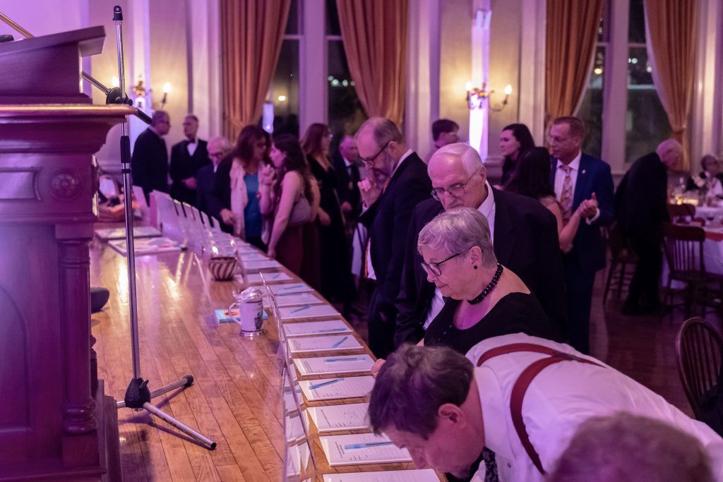 People lining up at a banquet table in a grand hall with purple lighting and tall curtains
