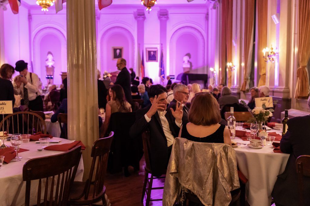 Elegant banquet hall with guests seated at round tables under purple lighting during a formal event