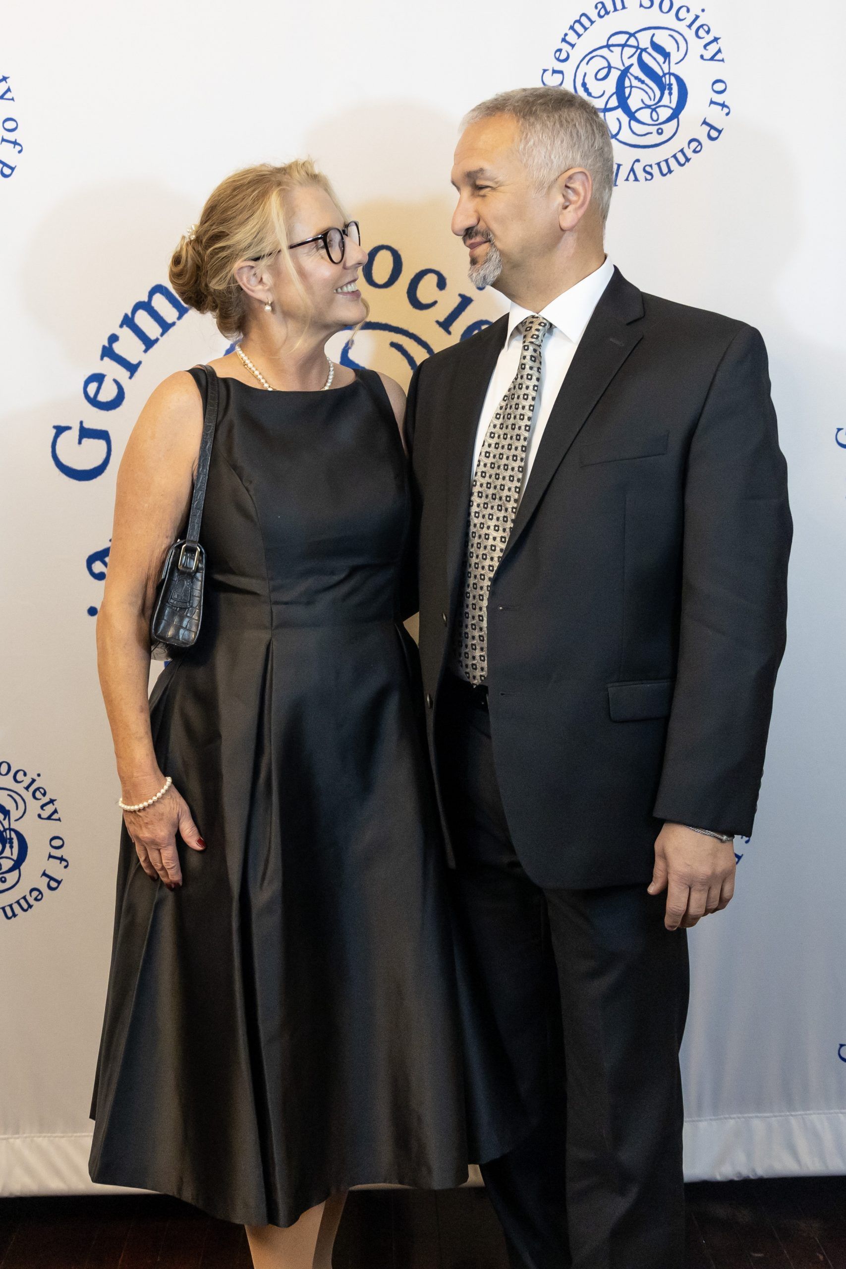 Two people posing in formal attire at a graduation ceremony backdrop