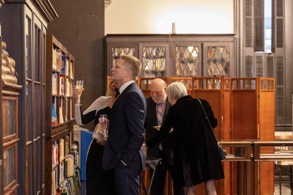 People browsing bookshelves in a quiet library with wooden furnishings and warm light