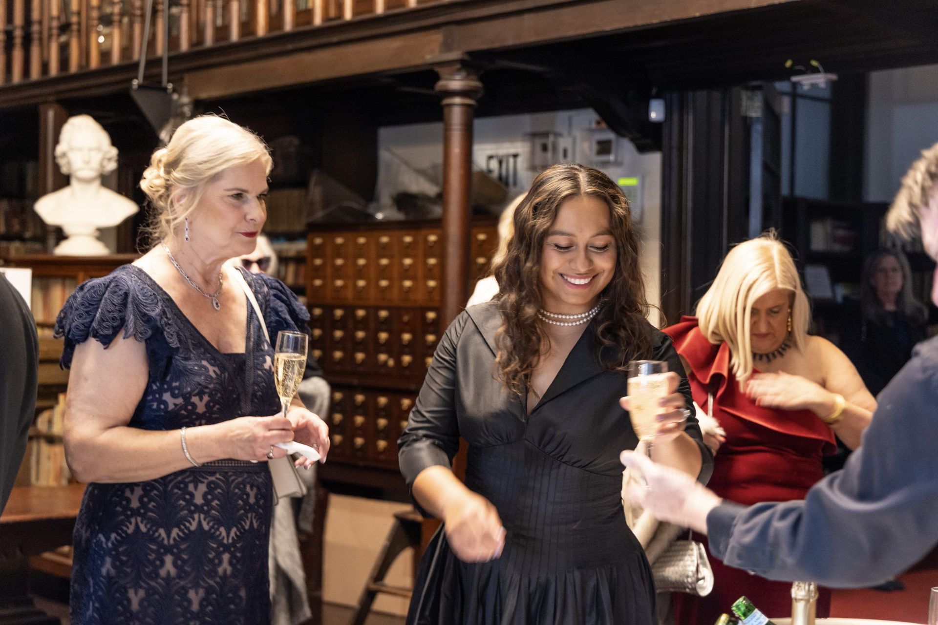 Three women chatting at a party, holding drinks in a dimly lit indoor venue