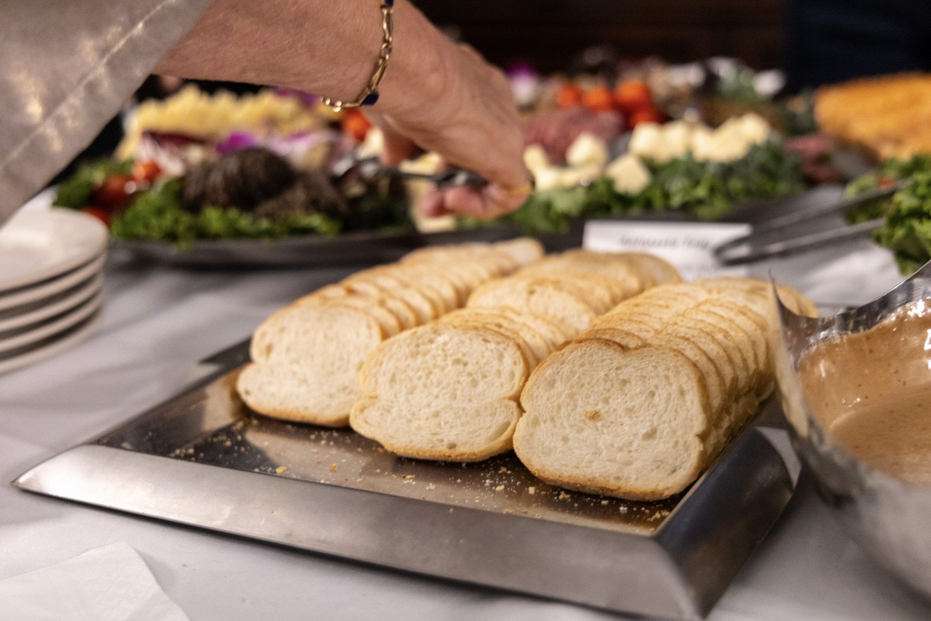 Sliced bread on a buffet tray with salads and a hand reaching for a serving utensil